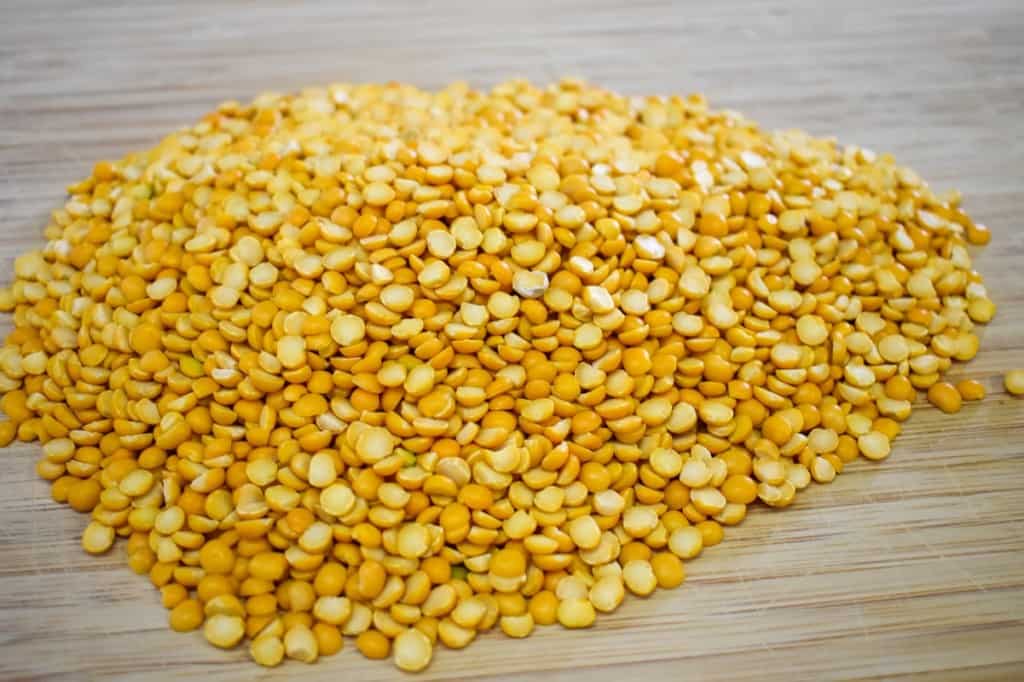 Dry yellow split peas on a wood cutting board.