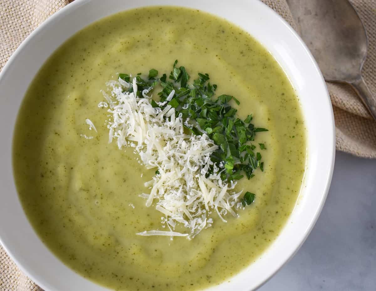 A close-up of the soup, garnished with chopped parsley and grated parmesan cheese, served in a white bowl.