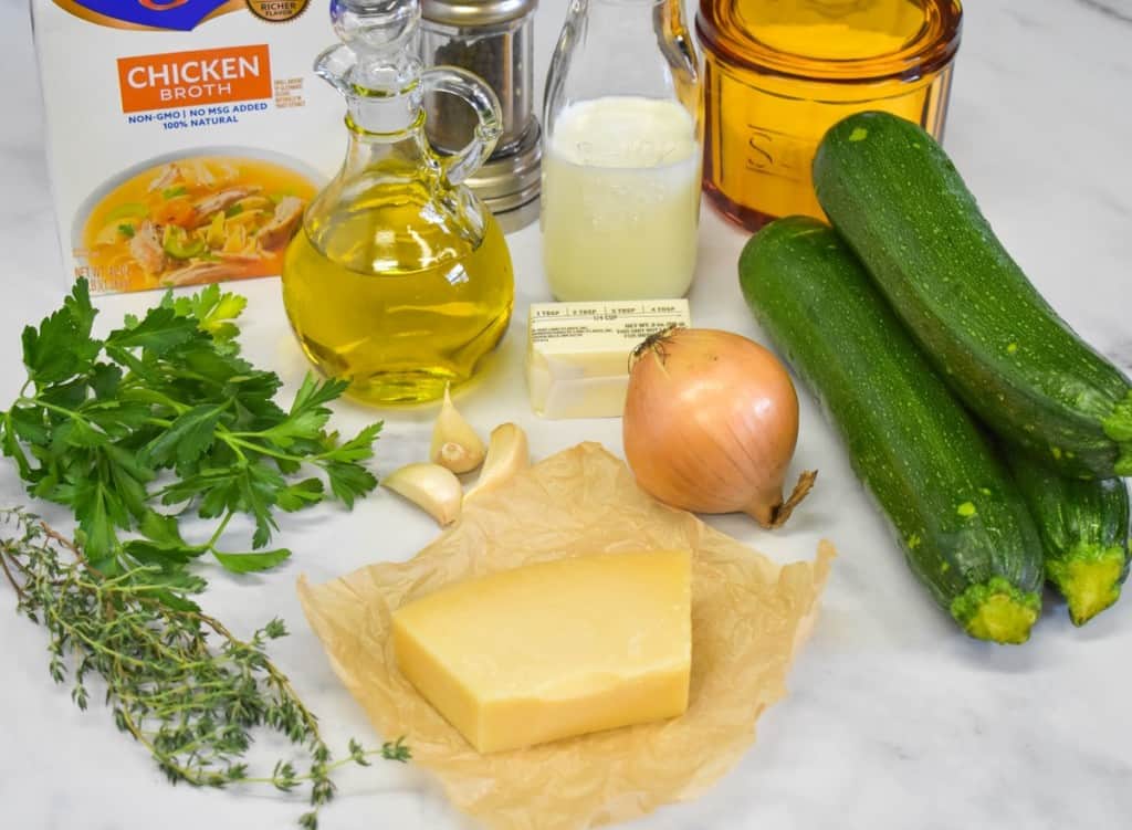 The ingredients for the zucchini soup arranged on a white table.