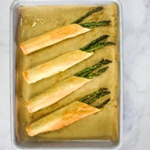 Four asparagus rolls set on a baking sheet lined with parchment paper.
