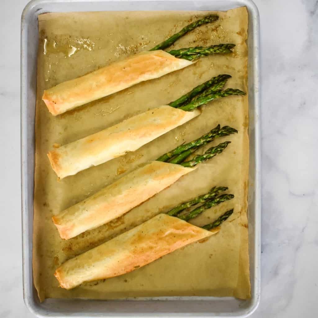 Four asparagus rolls set on a baking sheet lined with parchment paper.
