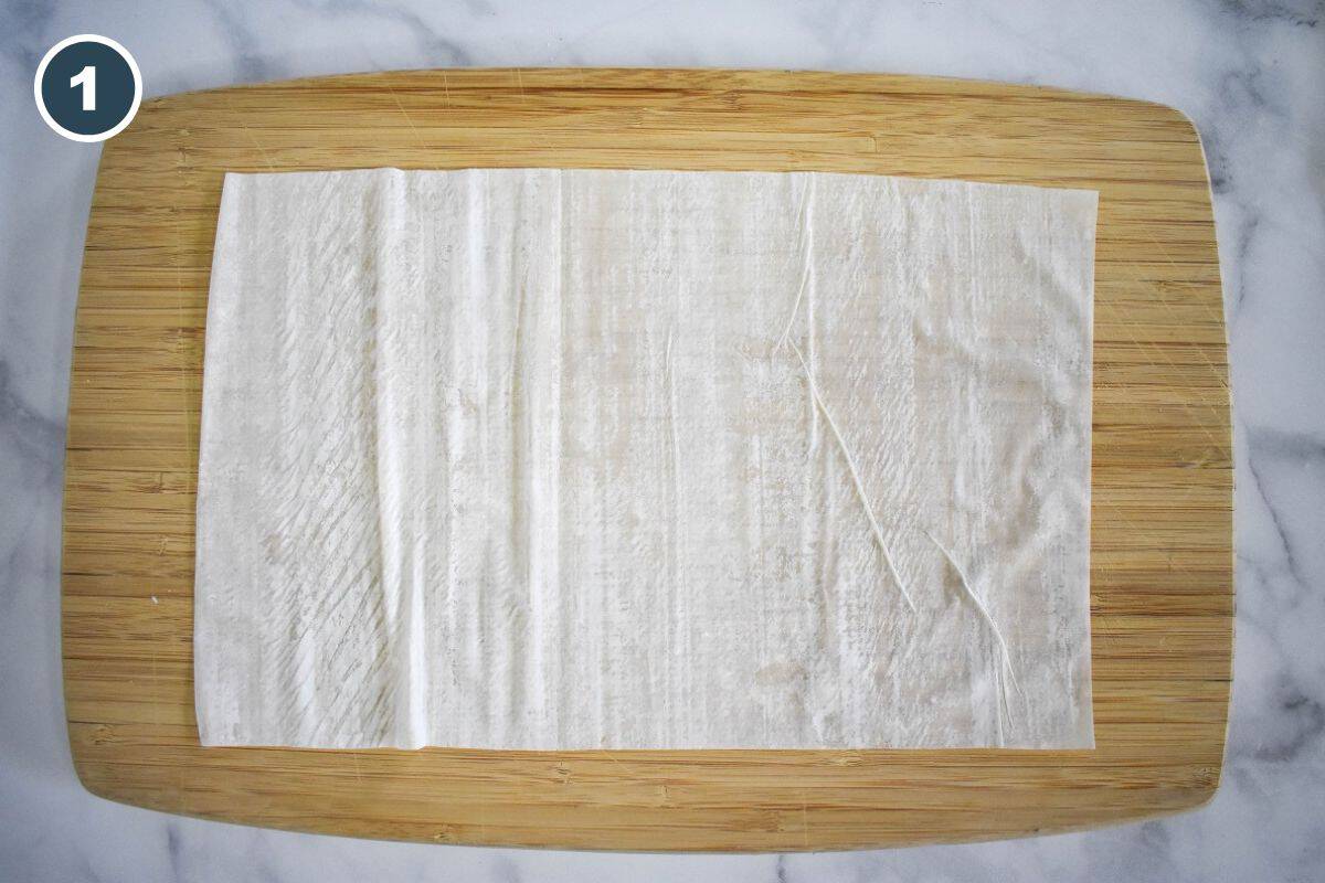 Laying a phyllo sheet on a wooden cutting board.