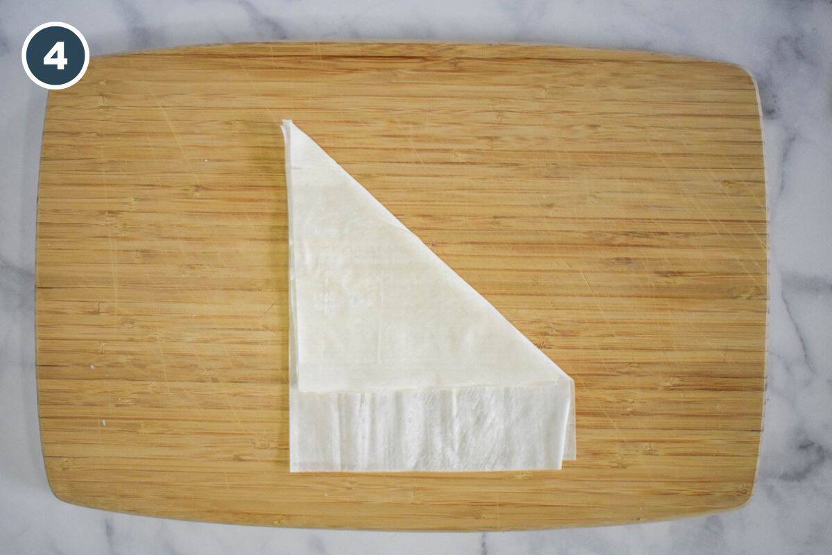 Folding one corner of the stacked phyllo to create a wedge shape.