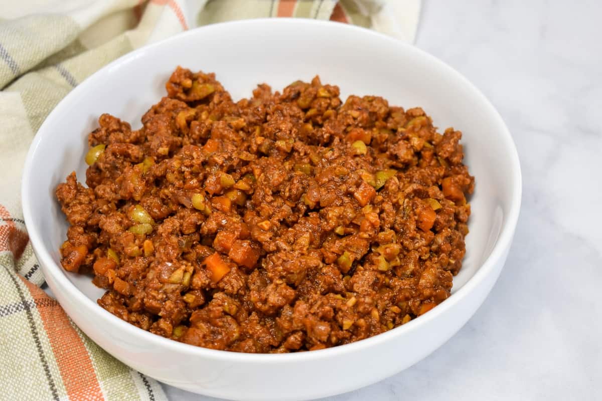 The ground turkey in a large white bowl set on a white table with a peach and beige kitchen towel to the left side.