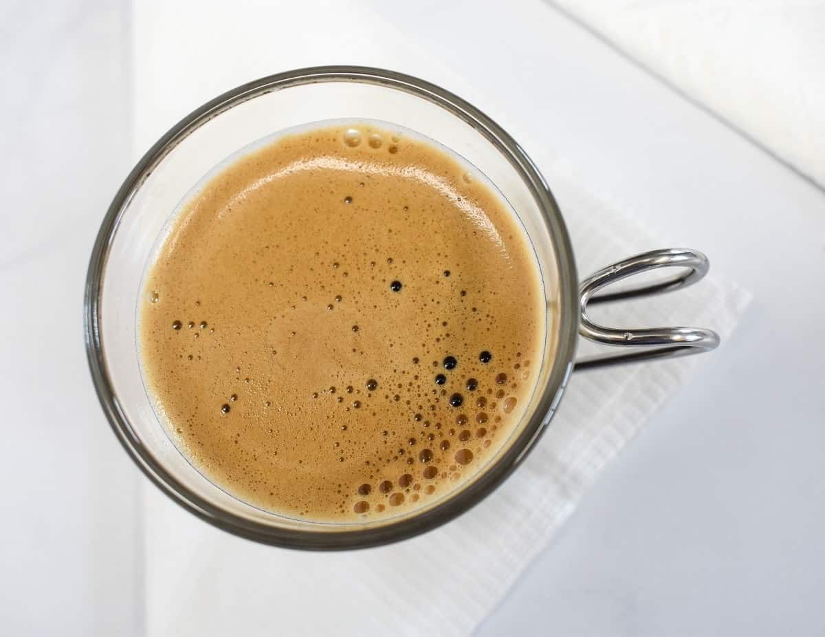 A top shot image of coffee in an espresso cup featuring the foam.