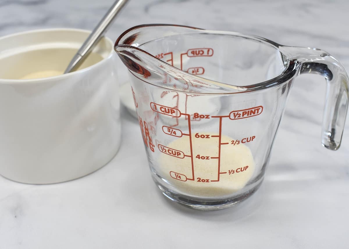 Sugar in a glass measuring cup with a sugar pot with a spoon in it on the left side.