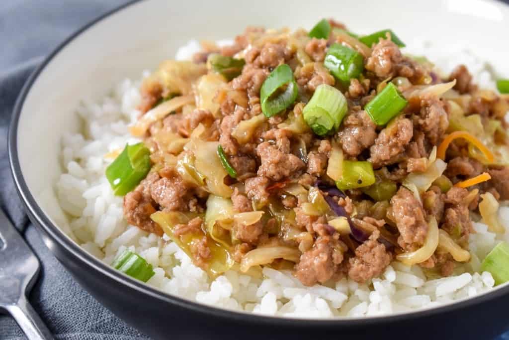 A close up image of the finished stir fry served on a bed of white rice in a white bowl.