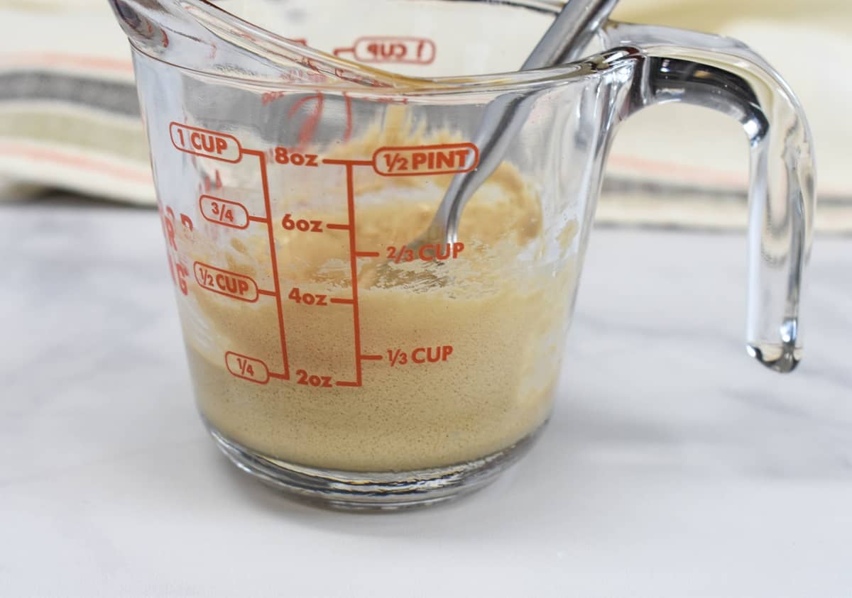 A glass measuring cup with the sugar coffee mixture beaten together to form a light beige mixture.