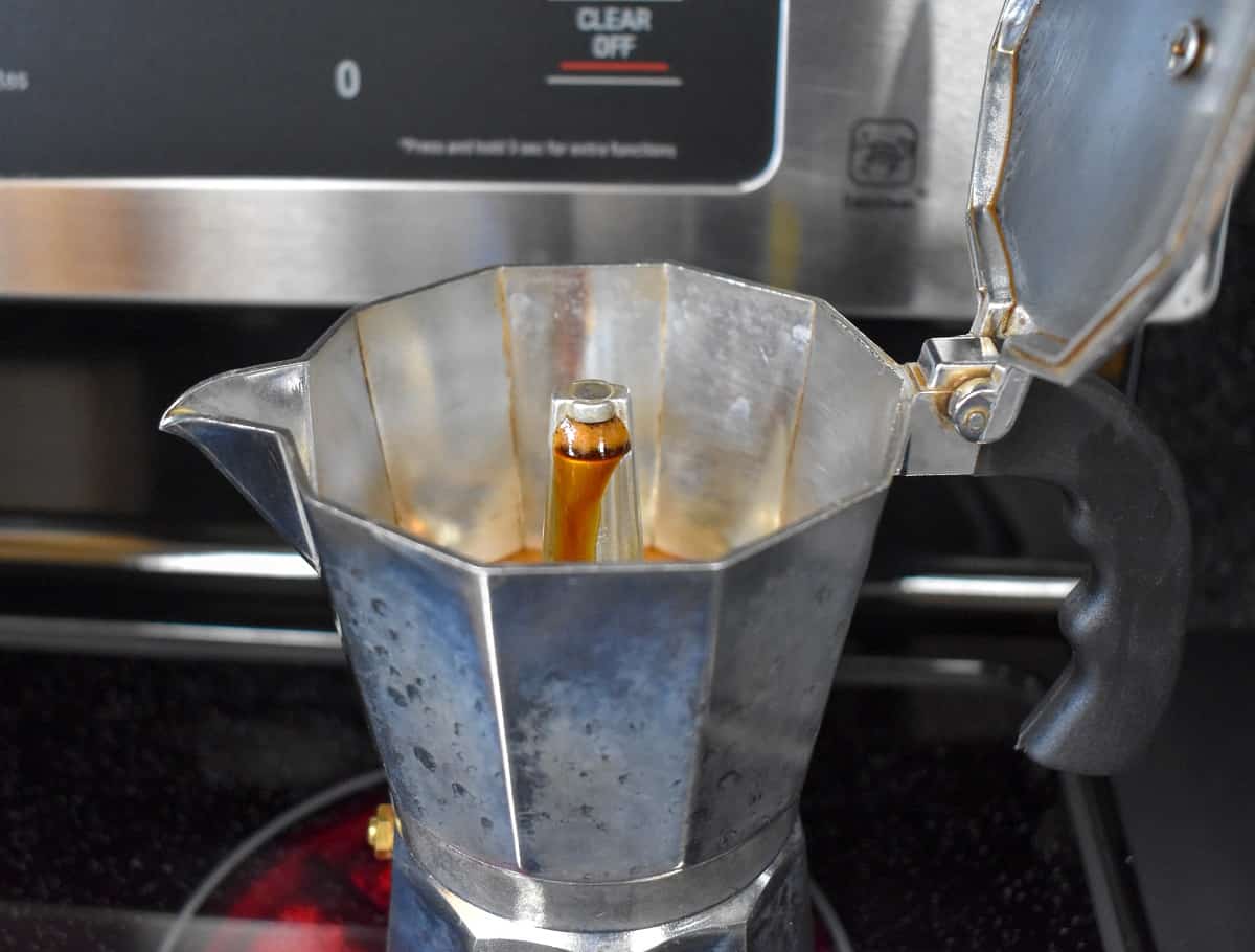 A close up of the stovetop coffee pot with coffee coming out of the brewing tip.