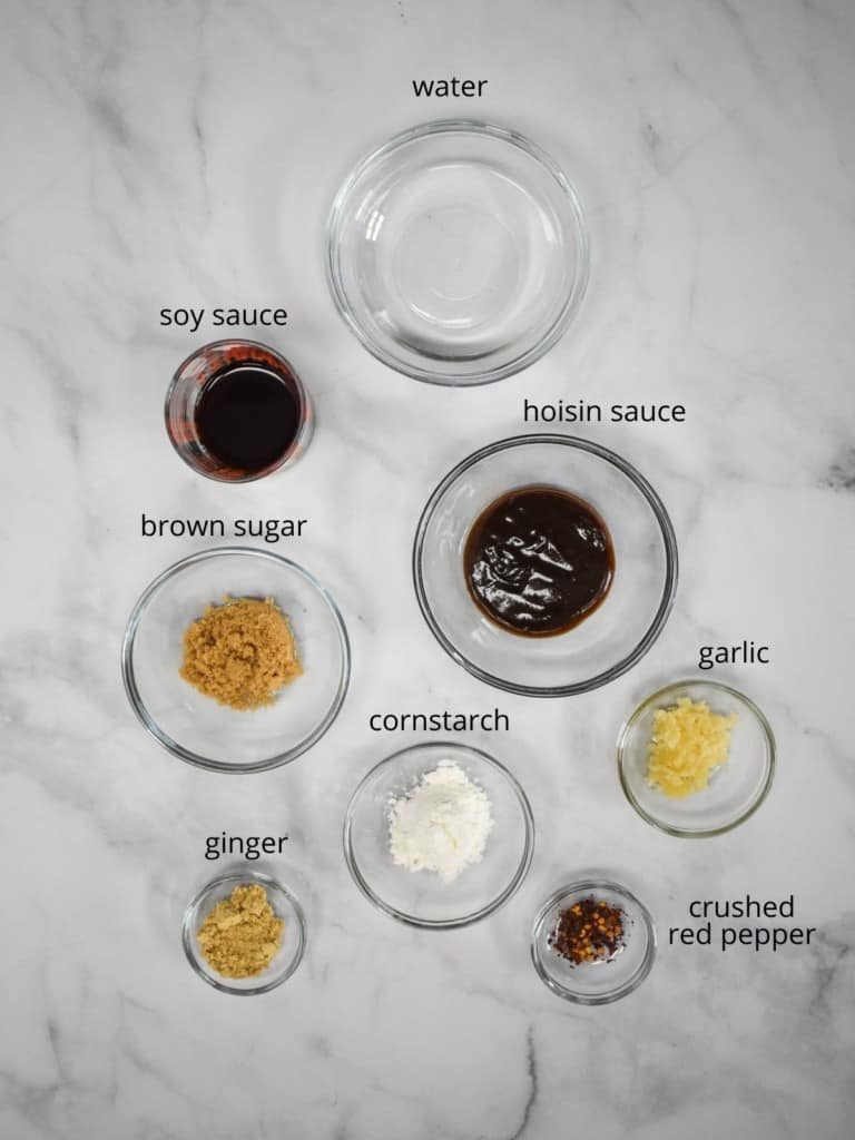 The ingredients for the stir fry sauce arranged in glass containers on a white table. Each ingredient has the name in small black letters next to it.