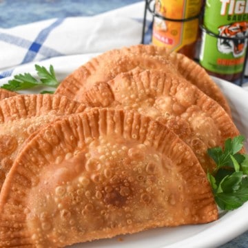 Four turkey empanadas arranged on a white platter and garnished with fresh parsley. In the back ground there are bottles of hot sauce.