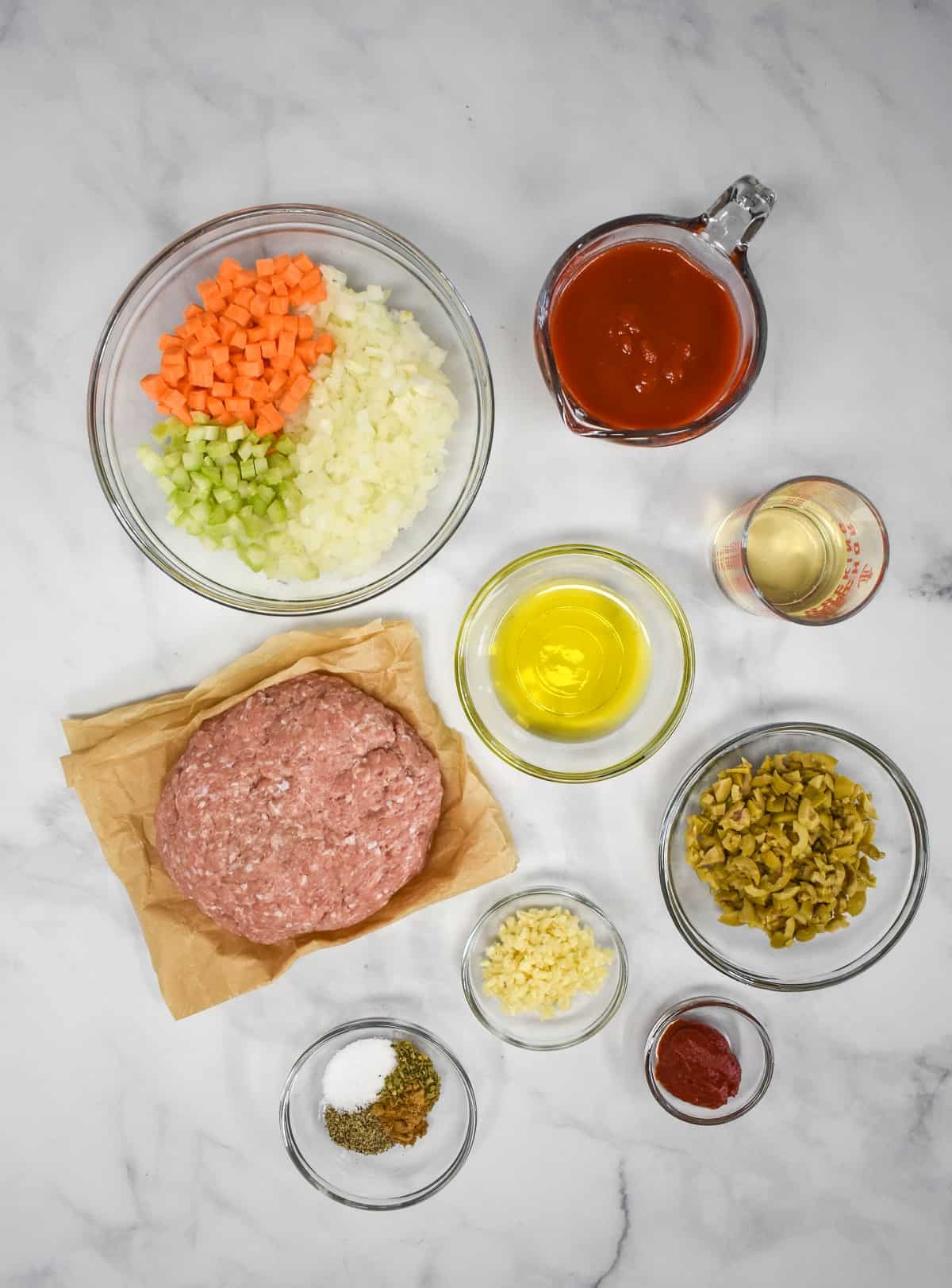 The prepped ingredients for the turkey picadillo filling arranged in glass bowls and arranged on a white table.