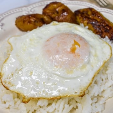 A close-up image of the arroz con huevo frito with sweet plantains served on an off-white plate.