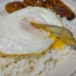 A close up of the arroz con huevo frito with a fork cutting into the yolk and served with sweet plantains.