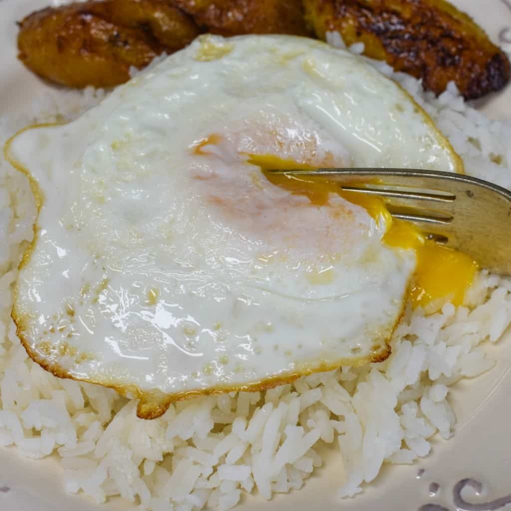 A close up of the arroz con huevo frito with a fork cutting into the yolk and served with sweet plantains.