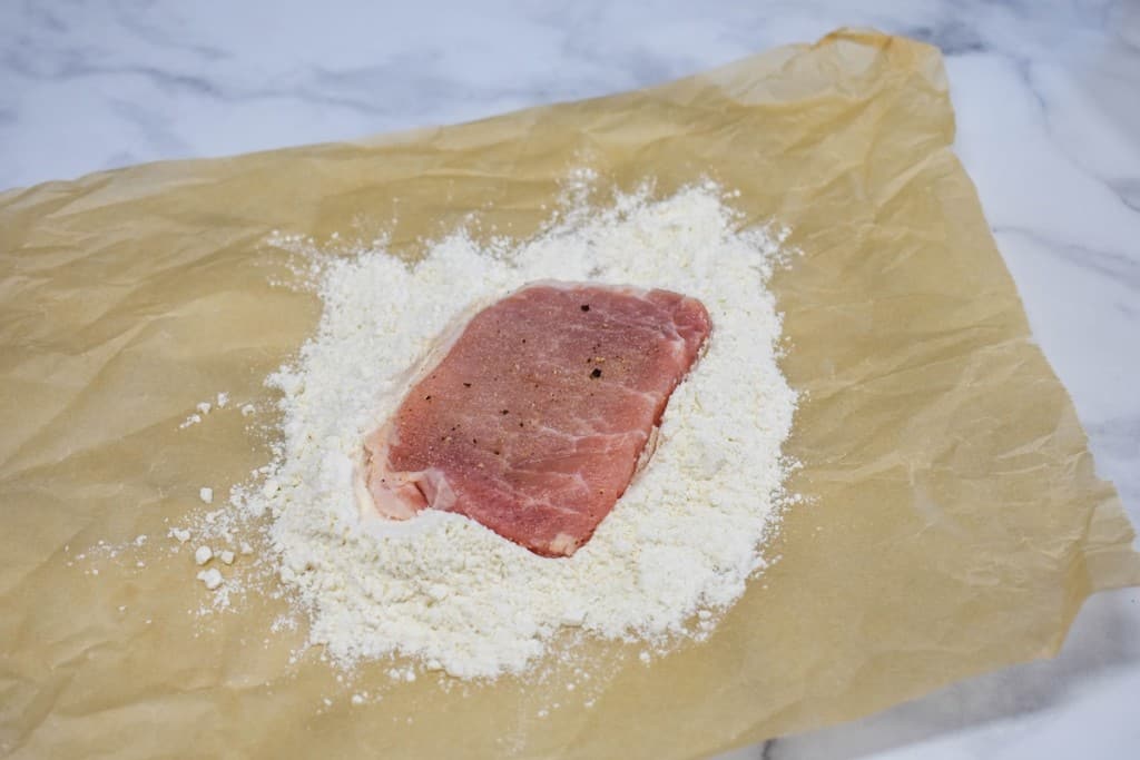 One boneless pork chop set in flour on a large piece of parchment paper.