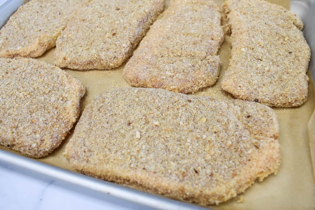 Breaded pork chops set on a baking sheet that's lined with parchment paper.