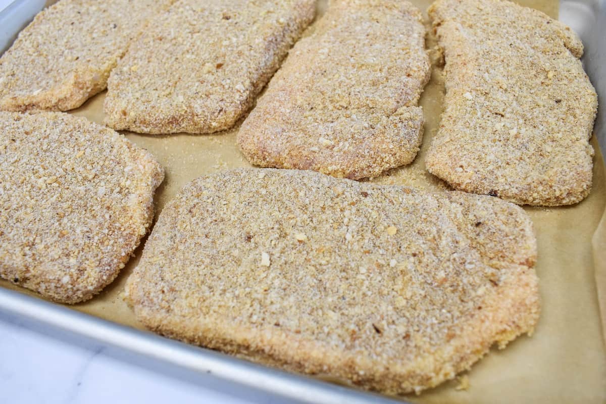 Breaded pork chops set on a baking sheet that's lined with parchment paper.
