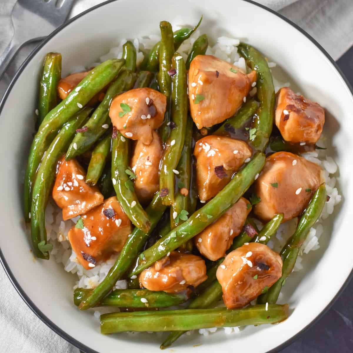 A close up of the chicken and green beans served over white rice in a white bowl with a black rim.