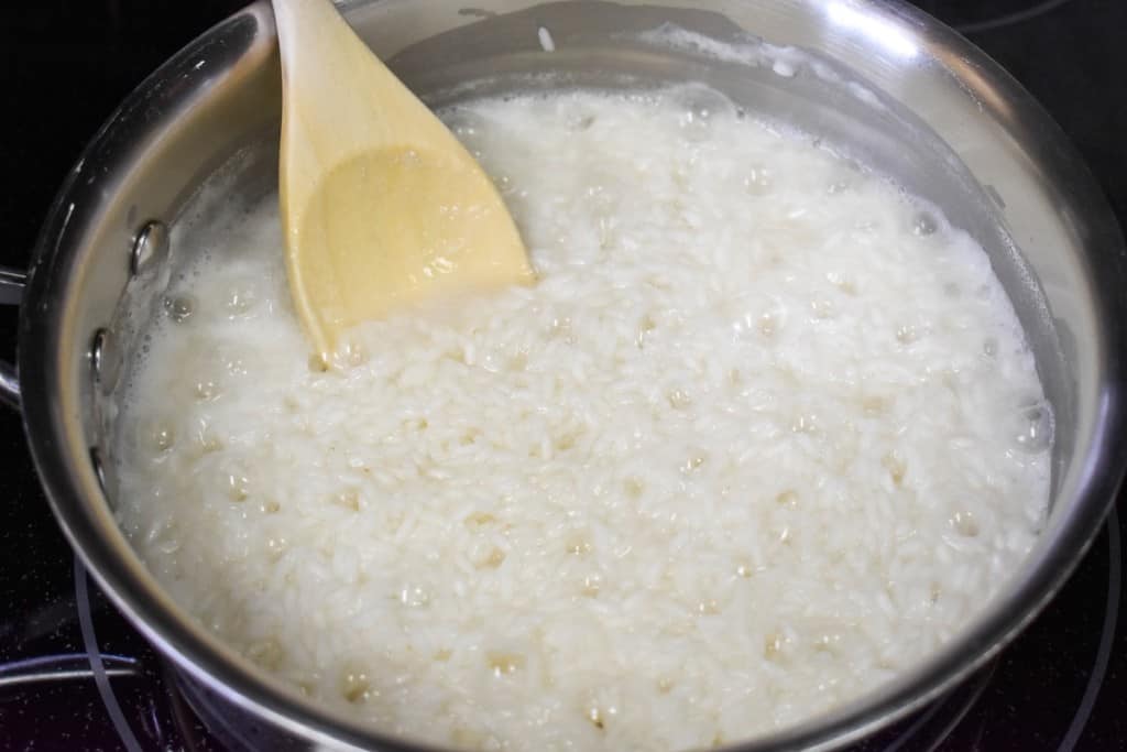 An image of cooking white rice in a saucepan with a wooden spoon in the pan.