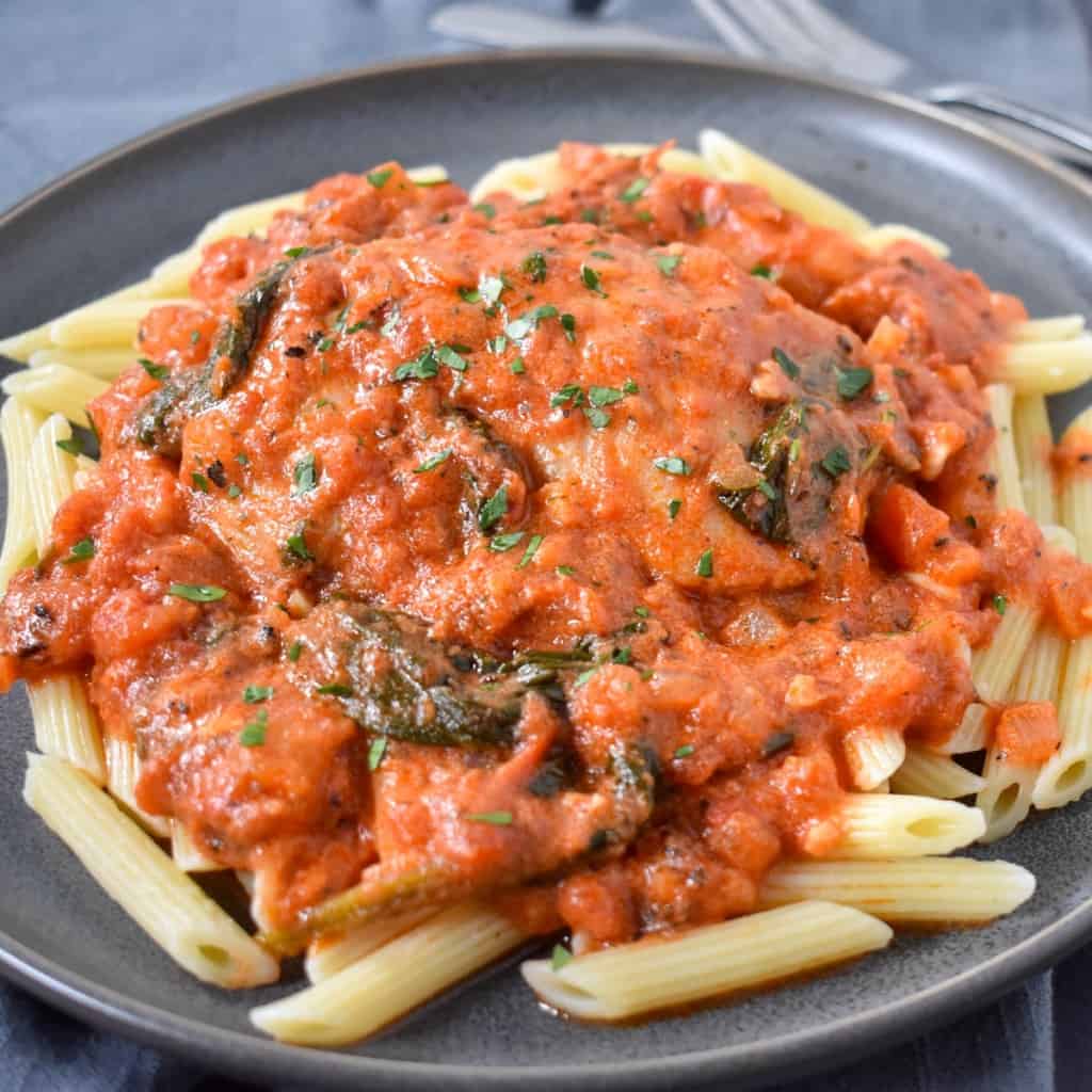 An image of the creamy tomato chicken on a bed of penne pasta served on a gray plate and garnished with chopped parsley.