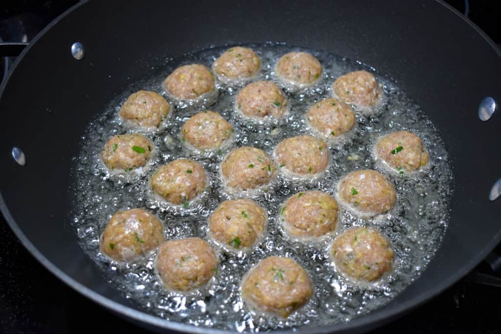 The meatballs in a large, black skillet frying in oil.