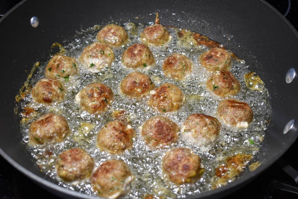 Frying meatballs in a large, black skillet with the browned side up.