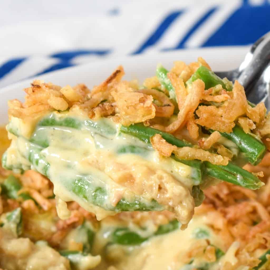 A close up image of a scoop of green bean casserole. There is a blue and white kitchen towel in the background.