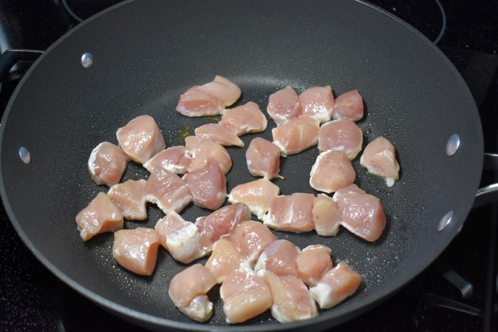 Bite sized chicken breast pieces arranged in a large, black skillet.