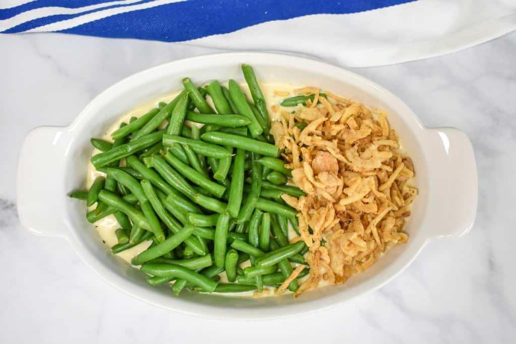 Green beans to the left and crispy fried onions to the right in a casserole dish before being stirred.