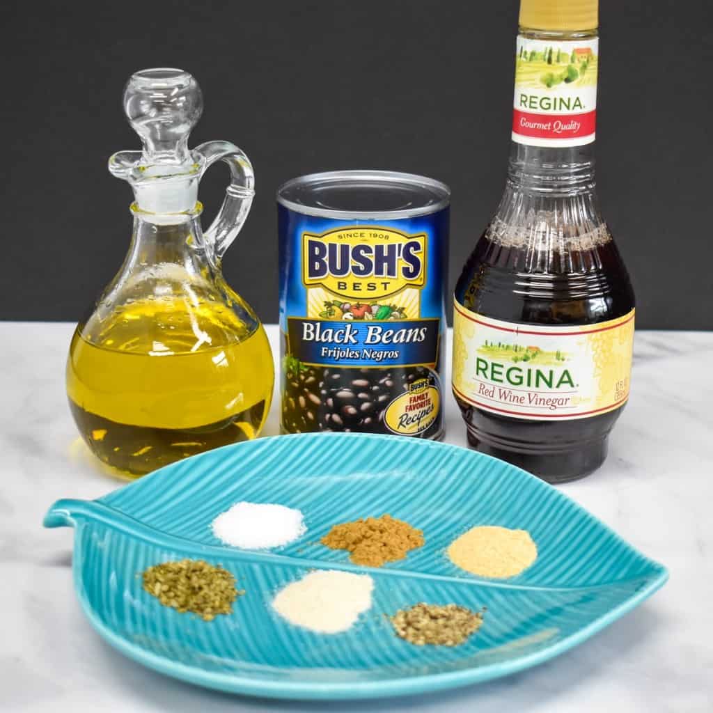 The ingredients for the quick Cuban style black beans on a white table with a black background. The spices are arranged in small piles on an aqua, leaf shaped plate.