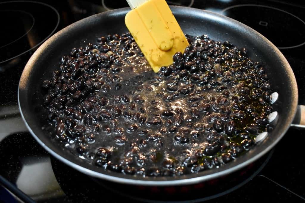 Black beans in a non-stick skillet being stirred with an orange rubber spatula.