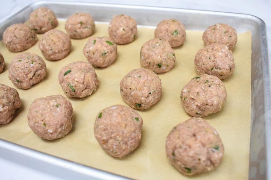 The formed turkey meatballs neatly arranged on a baking sheet that is lined with parchment paper.