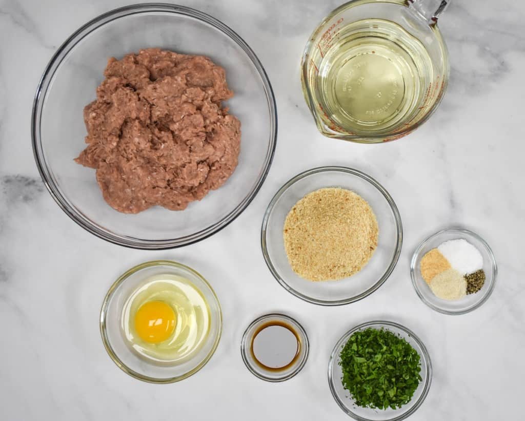 The ingredients for the meatballs, prepped and arranged in glass bowls on a white table.