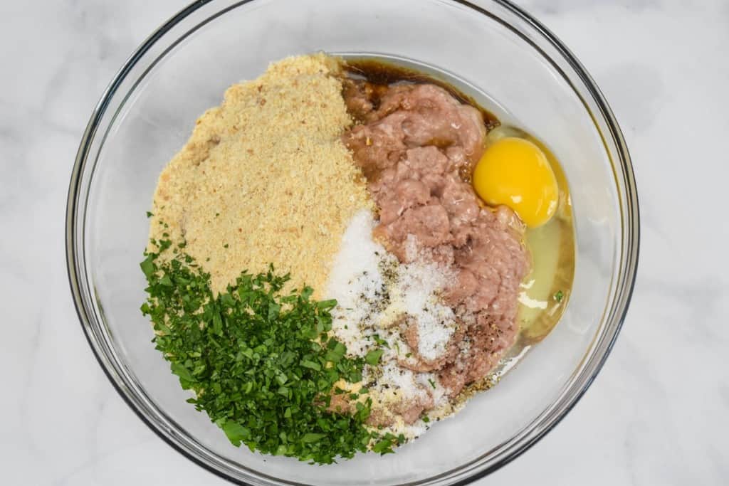 The ingredients for the meatballs added to a large, glass bowl but not yet combined.