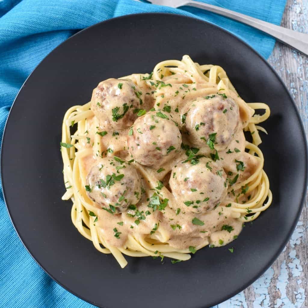 The turkey meatballs with gravy garnished with chopped parsley and served on a black plate and set on an aqua linen.