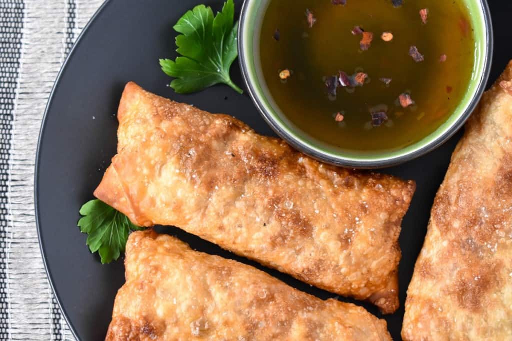 A close up image of the egg rolls set on a black plate with a small green bowl with sauce.