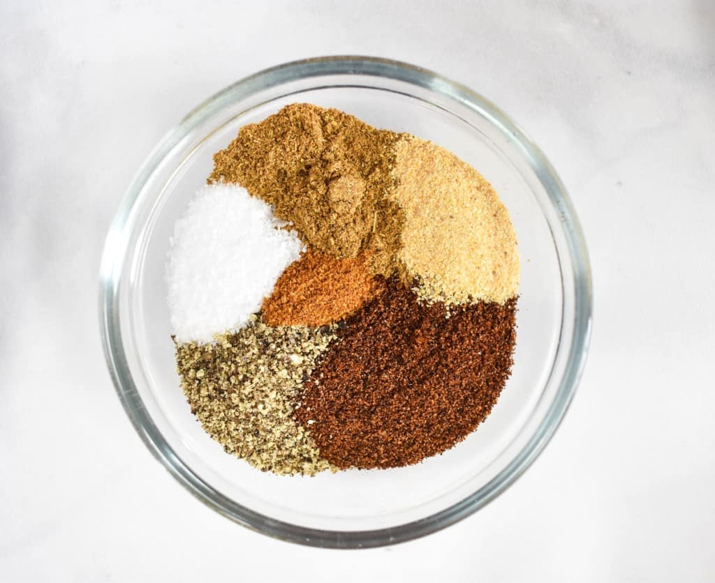 A close up image of the seasoning used in the recipe in a small glass bowl set on a white table.