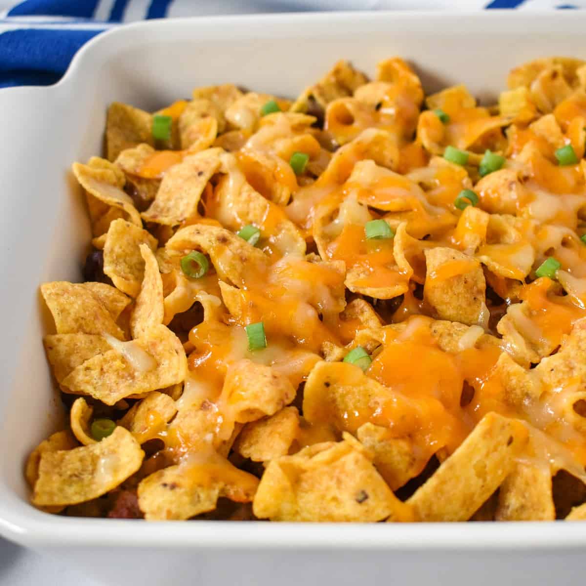 The finished frito pie in a white casserole dish and garnished with green onions.