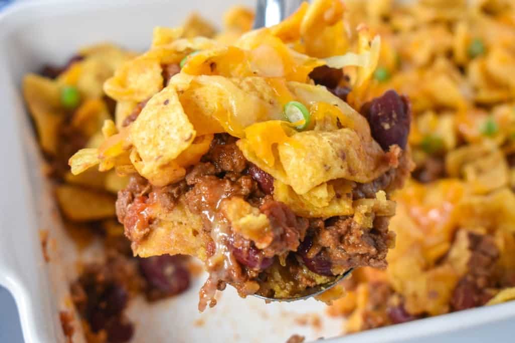 A scoop full of the frito pie held up with a serving spoon with the rest of it still in a white casserole dish.