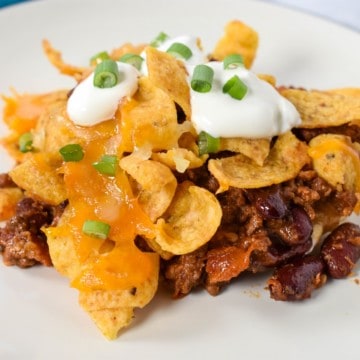 A serving of the frito pie served on a white plate and garnished with sour cream and sliced green onions.