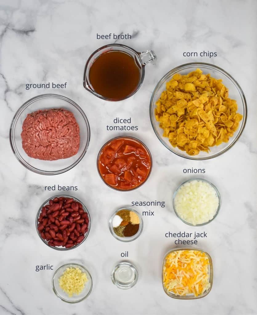 The ingredients for the dish, prepped and arranged in glass bowls on a white table. Each ingredient is labeled in small, letters.