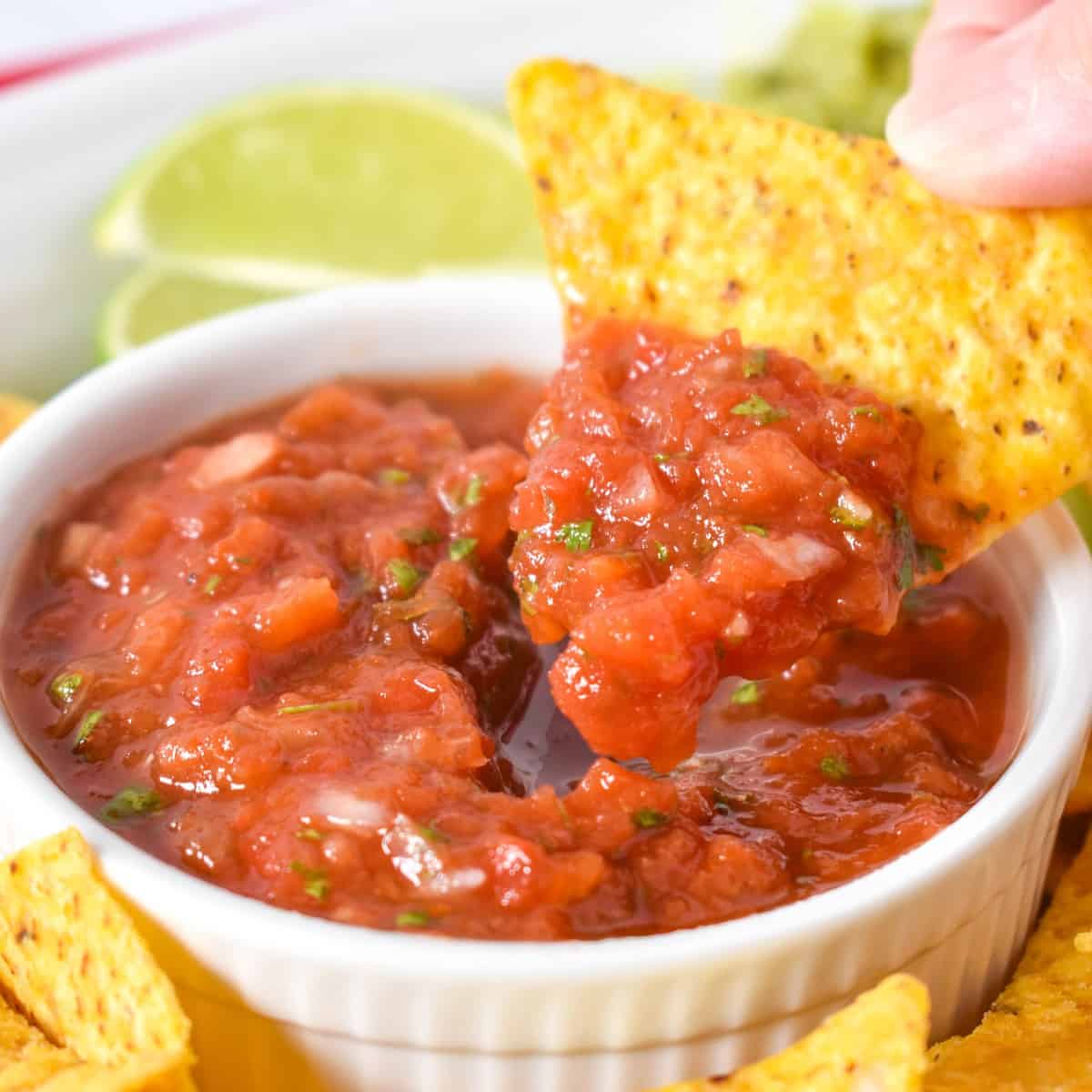 A close up image of a chip scooping some salsa out of a white bowl.