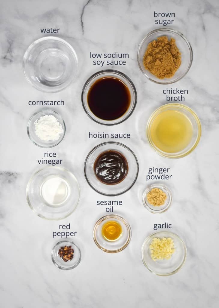 The ingredients for the sauce arranged in glass bowls and set on a white table. Above each ingredient is a label with its name.