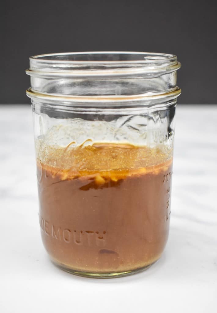 An image of the sauce for the sticky chicken thighs in a glass jar displayed on a white table.