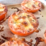 A close up of a baked tomatoes still on a parchment lined baking sheet.