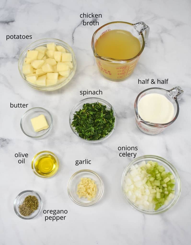 The ingredients for the cream of spinach soup prepped and arranged in glass bowls on a white table. Each ingredient has a label in small black letters.