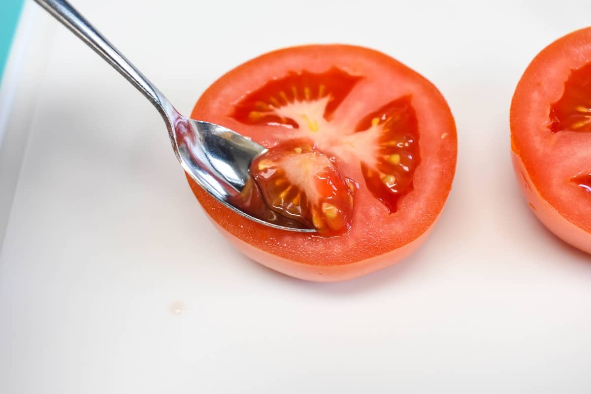 A small spoon removing the seeds from a tomato half.