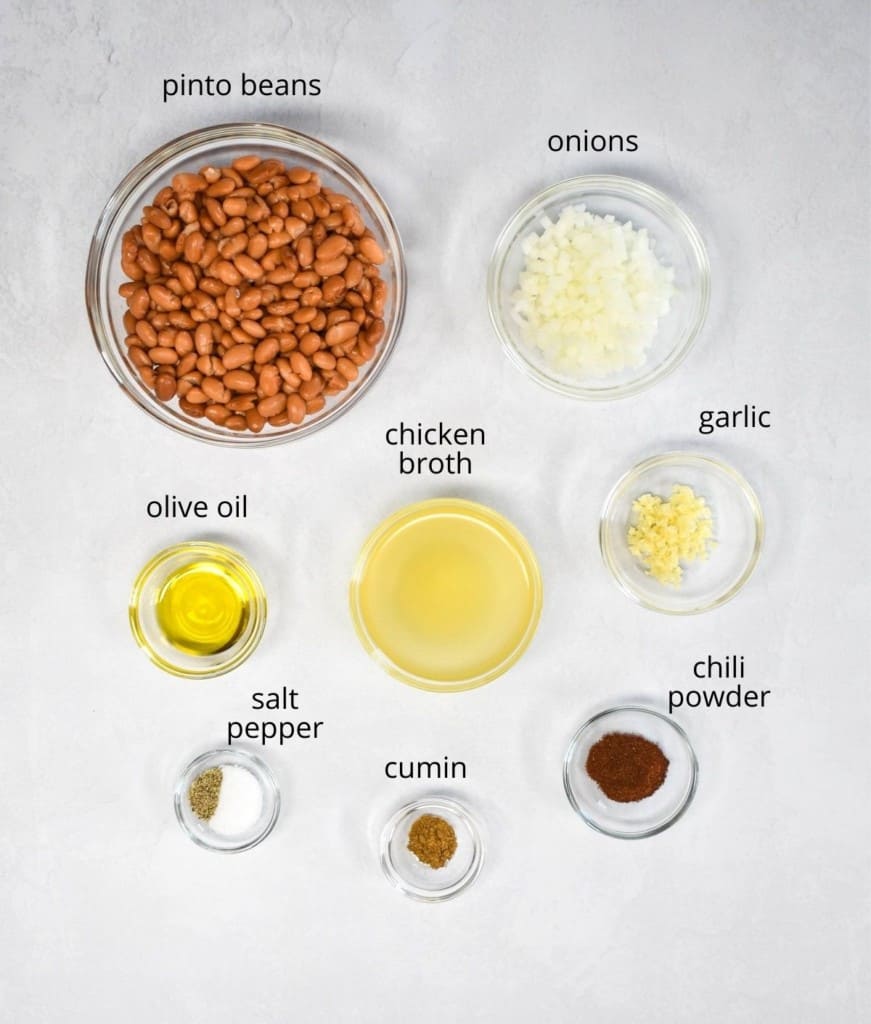 The ingredients for the refried beans, prepped and arranged in clear bowls on a white table.