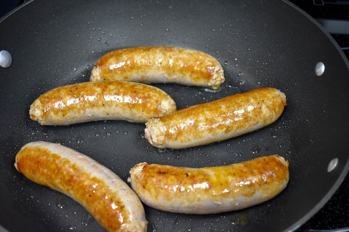 Italian sausage links browning in a nonstick skillet, golden on the outside.